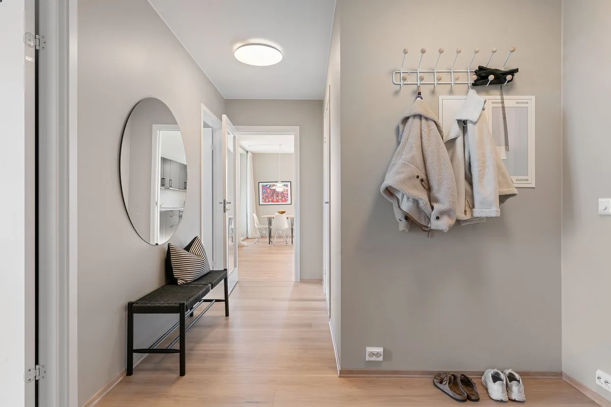 Minimalist apartment hallway with wall hooks, a slim bench, a round mirror, and shoes by the wall