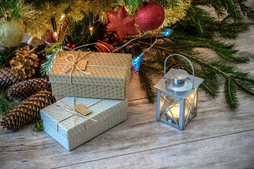 Kraft-wrapped Christmas gifts with twine, pinecones and a lantern under the tree