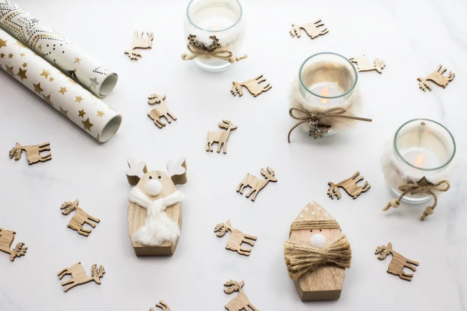 Rolls of white and gold wrapping paper with wooden reindeer and candle holders tied with twine